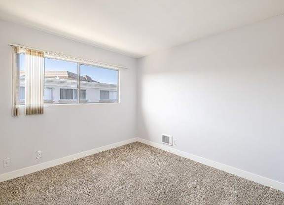 A room with a window and a carpeted floor.
