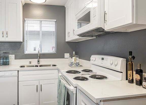 A white kitchen with a stove, sink, and cabinets.