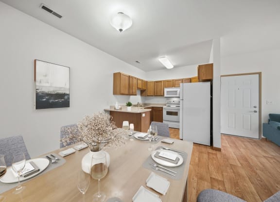 a dining area with a wooden table and chairs and a kitchen in the background
