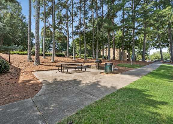 A park with a bench and a trash can.