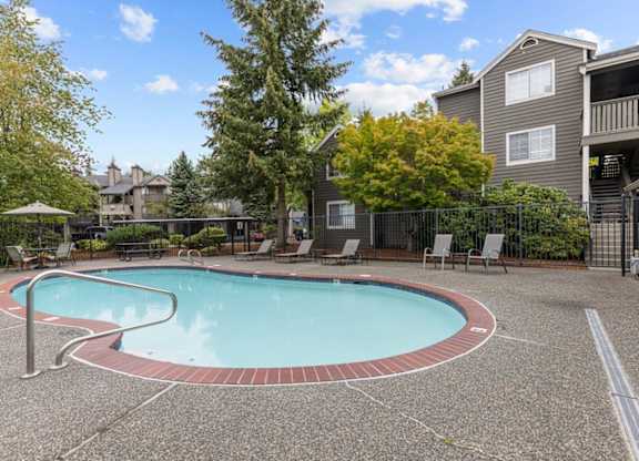 a swimming pool with chairs and a building in the background
