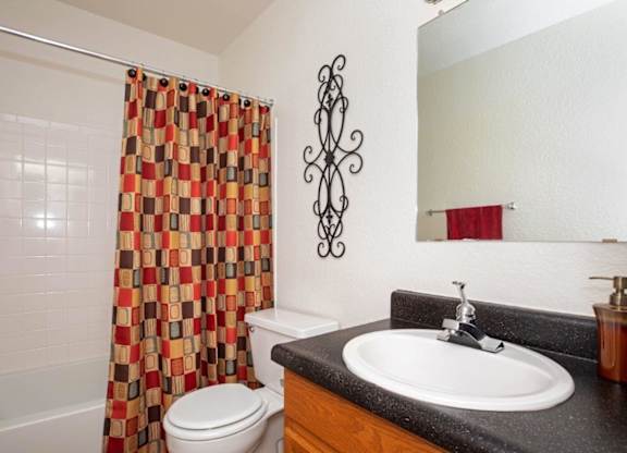 A bathroom with a white toilet, a black counter top, and a shower curtain with a pattern of squares and rectangles.