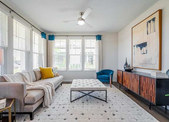 A living room with a grey couch, a blue chair, a white coffee table, and a painting on the wall.
