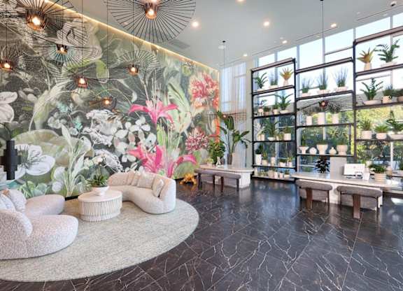 A living room with a large floral mural on the wall and a variety of plants on shelves.
