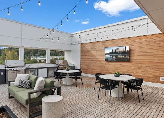 A patio with a table, chairs, and a couch with a view of trees and a house in the distance at Cru at Willows Apartments, Redmond, 98052