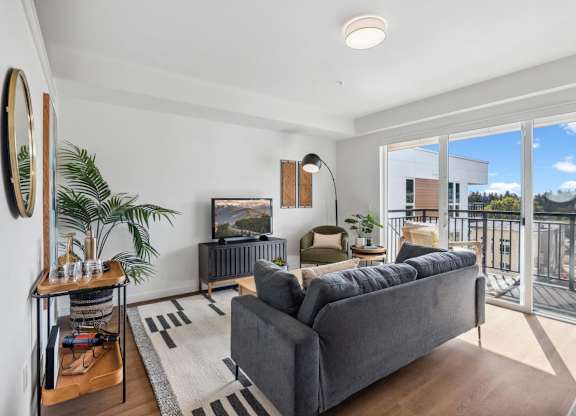 A living room with a grey couch and a flat screen TV at Cru at Willows Apartments, Redmond, Washington, 98052