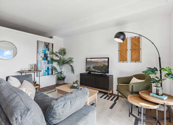 A living room with a grey couch, a green armchair, a wooden coffee table, and a television at Cru at Willows Apartments, Washington