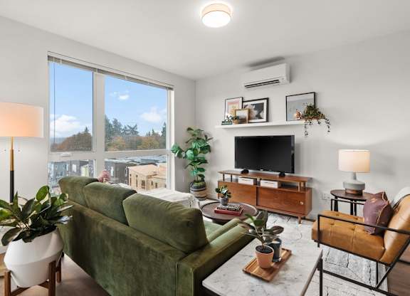 A living room with a green couch, a television, and a Air conditioner at Cru at Willows Apartments, Redmond, WA, 98052