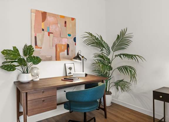 A painting hangs on the wall above a desk with a chair and a plant at Cru at Willows Apartments, Redmond, Washington