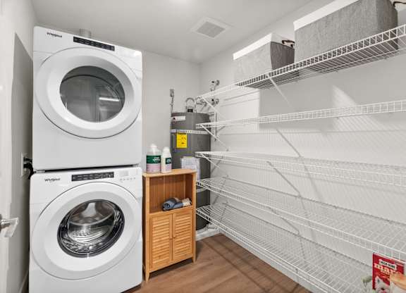 A white dryer is in a laundry room with a shelf and racks at Cru at Willows Apartments, Washington