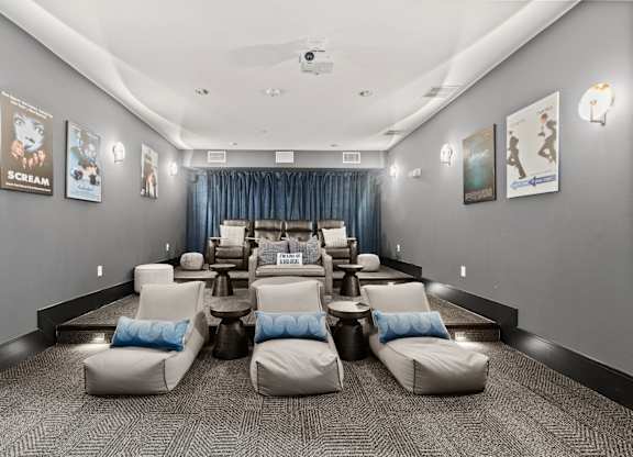 A room with grey walls and a carpeted floor has a row of white chairs with blue pillows.