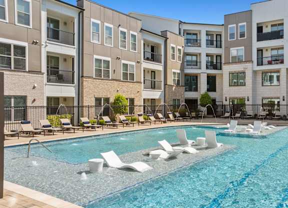 A large swimming pool with lounge chairs in front of apartment buildings.