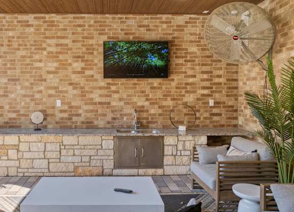 A modern outdoor living space with a brick wall and a television mounted above a fireplace.
