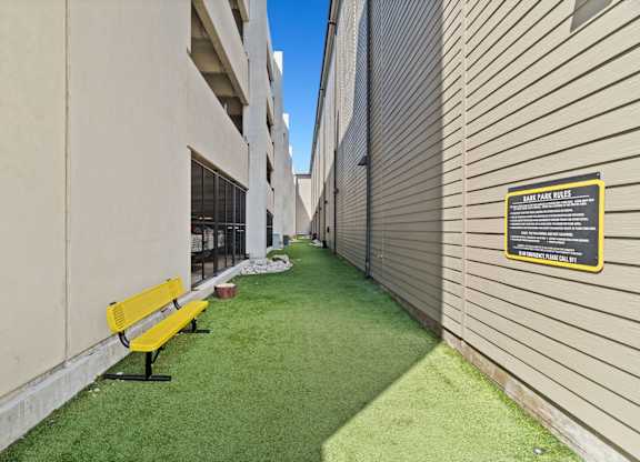 A yellow bench sits on a green lawn next to a building.