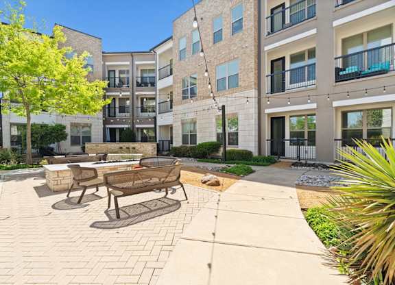 A sunny day at a modern apartment complex with a brick patio and seating area.
