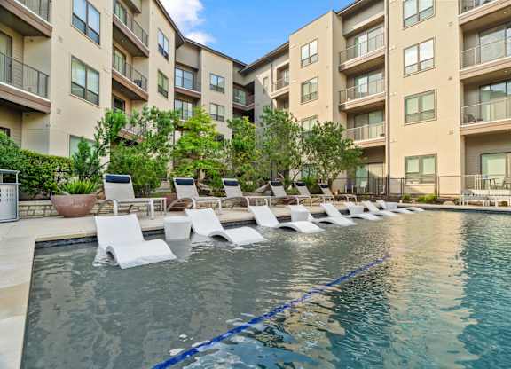 A pool with lounge chairs in front of apartment buildings.