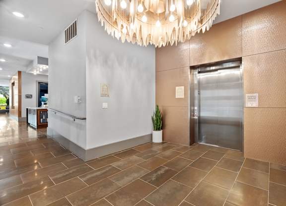 A large, modern chandelier hangs over a reception desk in a well-lit hallway.