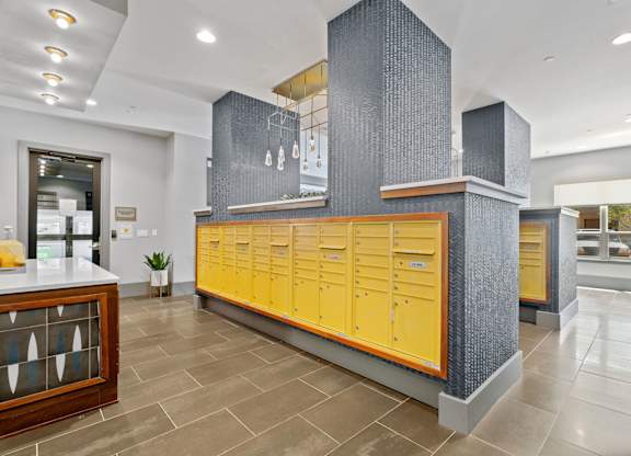 A row of yellow lockers are in a room with a grey column and a counter.
