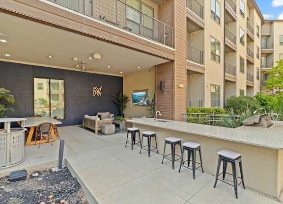 A patio with a bar and stools is surrounded by apartment buildings.