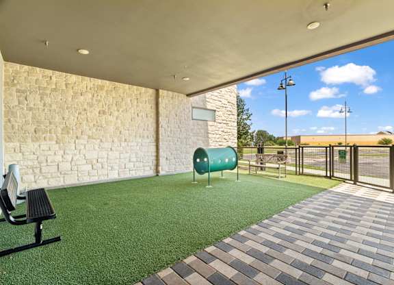 A patio area with a bench, a green trash can, and a brick wall.
