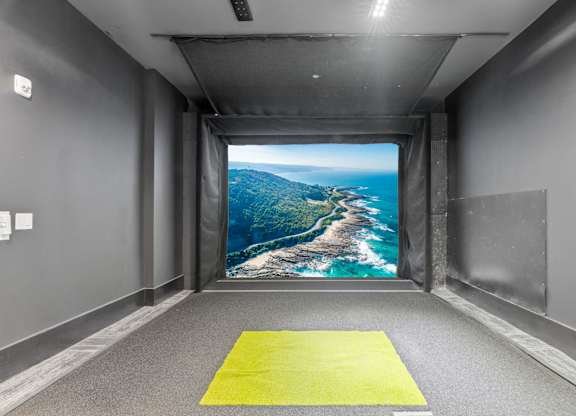 A bright yellow mat is on the floor of a room with a large picture of a coastline on the wall.