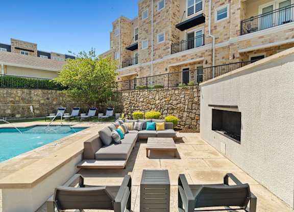 A poolside patio with chairs and a stone wall.
