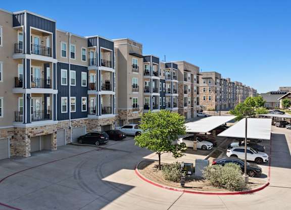 A view of apartment buildings with cars parked in the driveway.