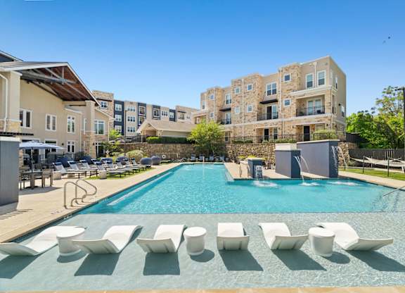 A swimming pool with sun loungers in front of apartment buildings.