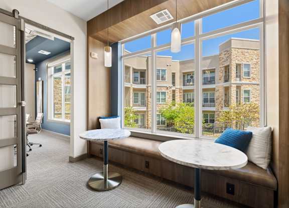 A room with a table and a bench with a view of a building outside.