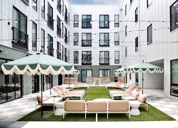 A patio with white furniture and green umbrellas is surrounded by white buildings.
