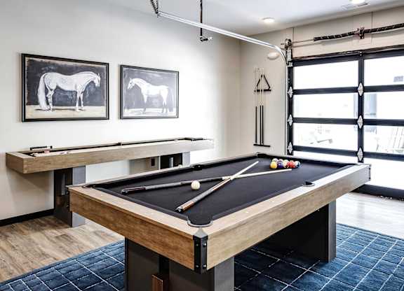 A pool table in a room with two framed horse pictures on the wall.