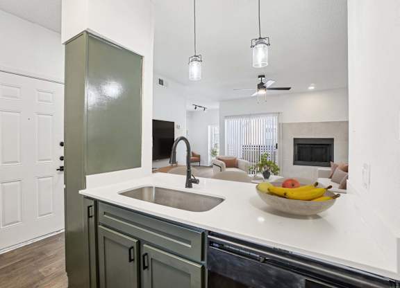 A kitchen with a sink and a bowl of fruit on the counter.