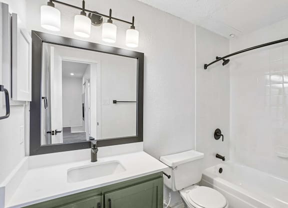 A white bathroom with a green cabinet and a black framed mirror.