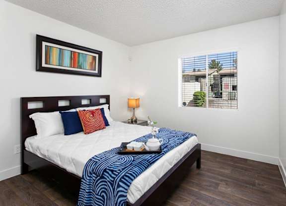A bedroom with a bed, nightstand, and a window with a view of a building and trees.