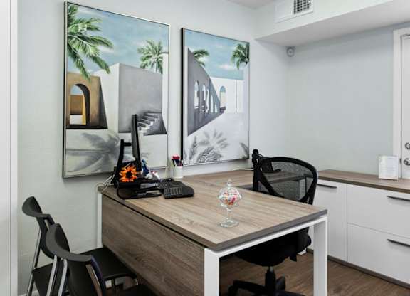 A room with a desk, chairs, and two paintings on the wall.