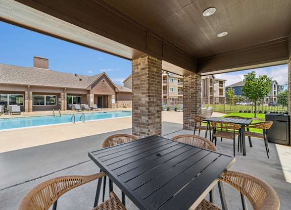 A black table is in the middle of a patio with chairs around it.