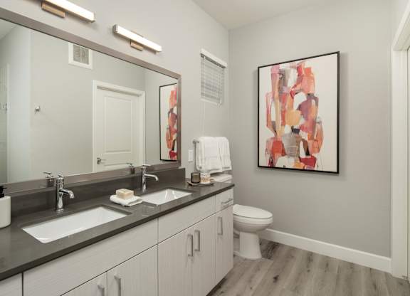 A bathroom with a large mirror, a sink, a toilet, and a painting on the wall.