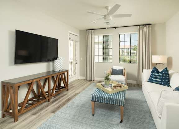 A living room with a white couch, a wooden coffee table, and a flat-screen TV mounted on the wall.