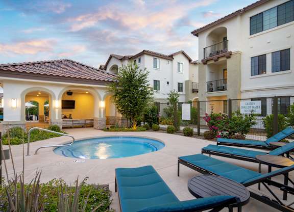 A pool surrounded by lounge chairs and a building with a balcony.