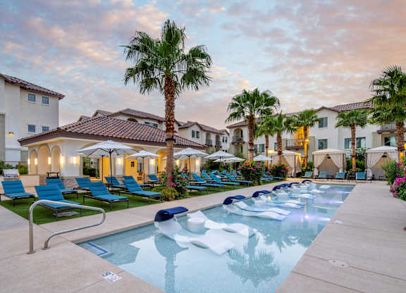 A pool surrounded by palm trees and lounge chairs.