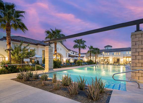 A pool surrounded by palm trees and a building in the background.