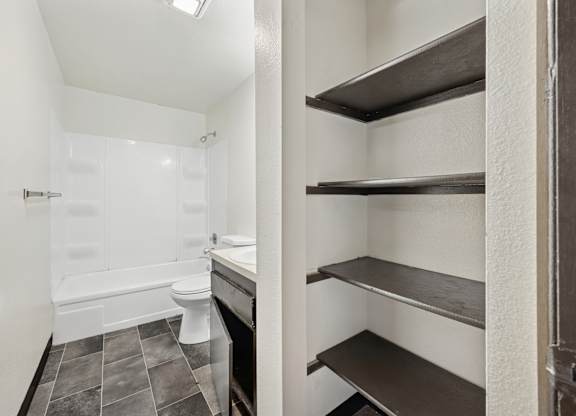 A white bathroom with a toilet, sink, and shelves.