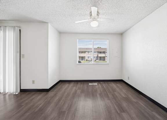 A room with a ceiling fan and a window showing a building outside.