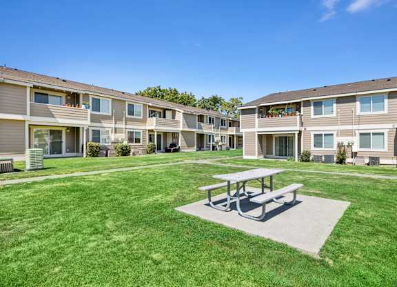 A large grassy area with a picnic table in the middle of apartment buildings.