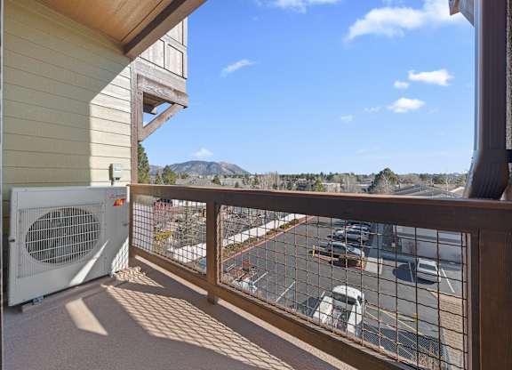 A balcony with a fan and a view of a parking lot and mountains.