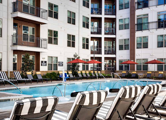 a swimming pool with lounge chairs and umbrellas in front of a building