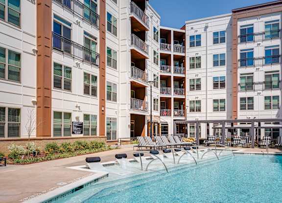 an outdoor swimming pool with chaise lounge chairs and a building in the background
