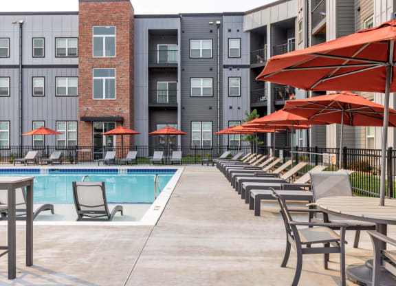 a swimming pool with chairs and umbrellas in front of an apartment building