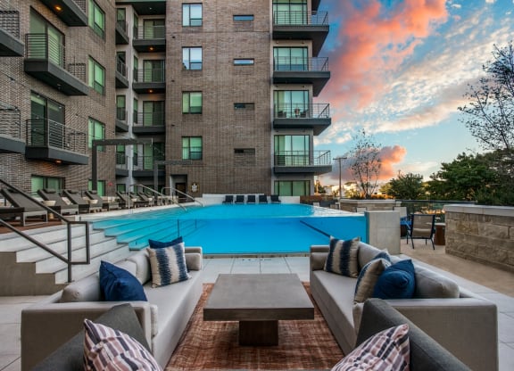 an outdoor lounge area with couches and a coffee table in front of an apartment building