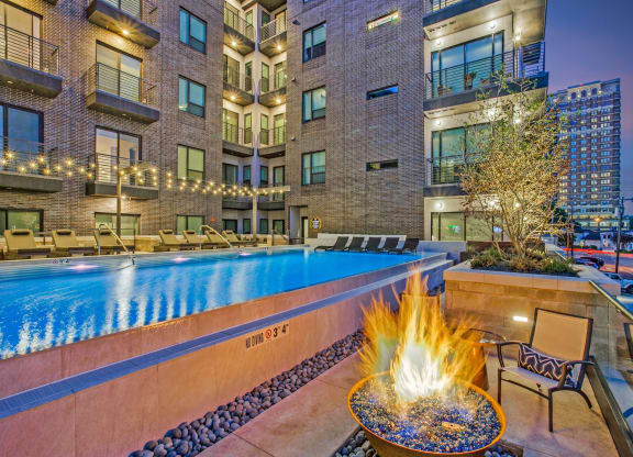 a pool with a fire pit and lounge chairs in front of an apartment building